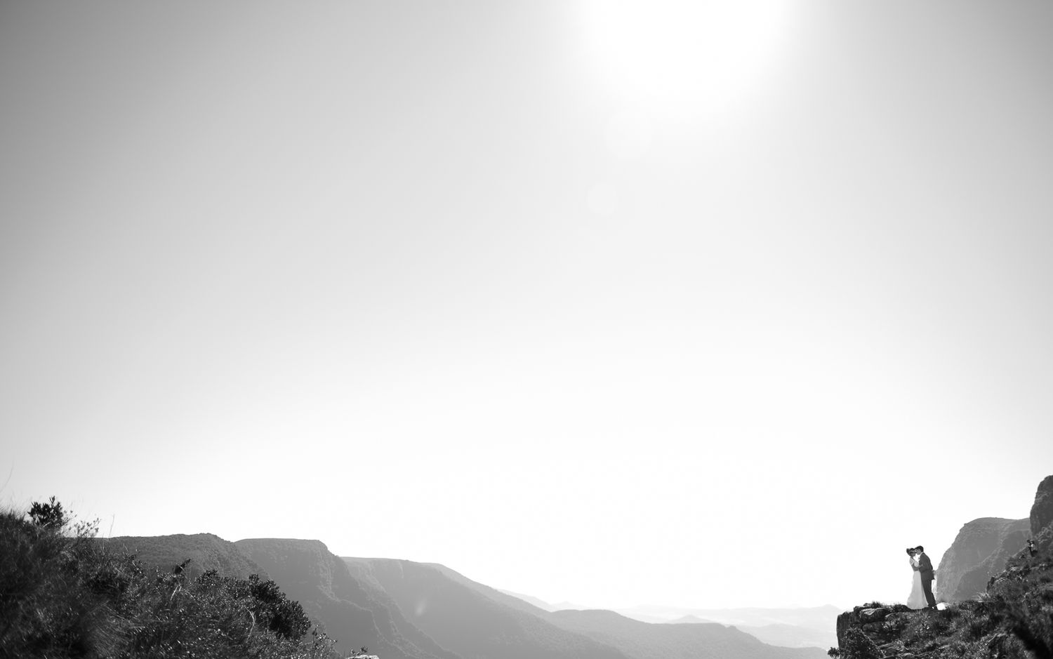 A silhouetted figure stands atop a mountain ridge against a bright sky.