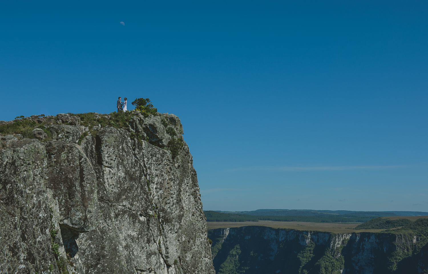 A dramatic cliffside view with distant figures perched on the rocky edge.