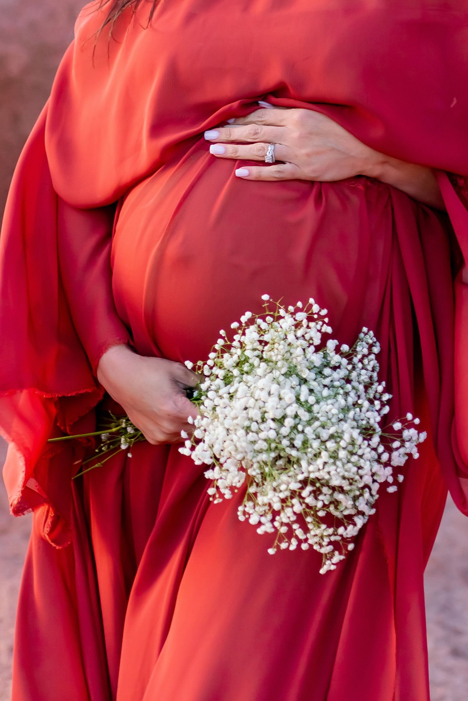 A close-up of a pregnant belly in red dress holding delicate baby's breath flowers.