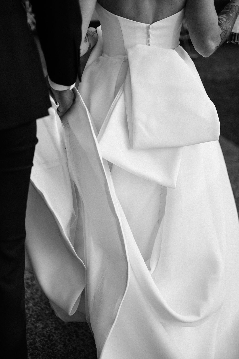 Black and white photo of a bride in a stunning structured ball gown with dramatic bow detail, held by groom.