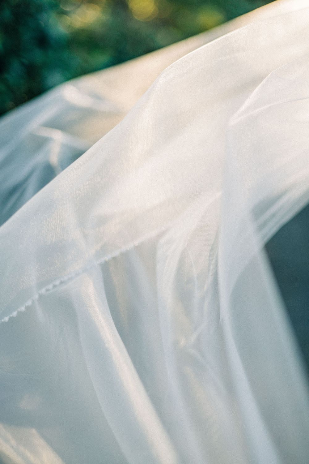 Flowing white bridal veil billowing in the breeze against a soft green bokeh background in natural light.