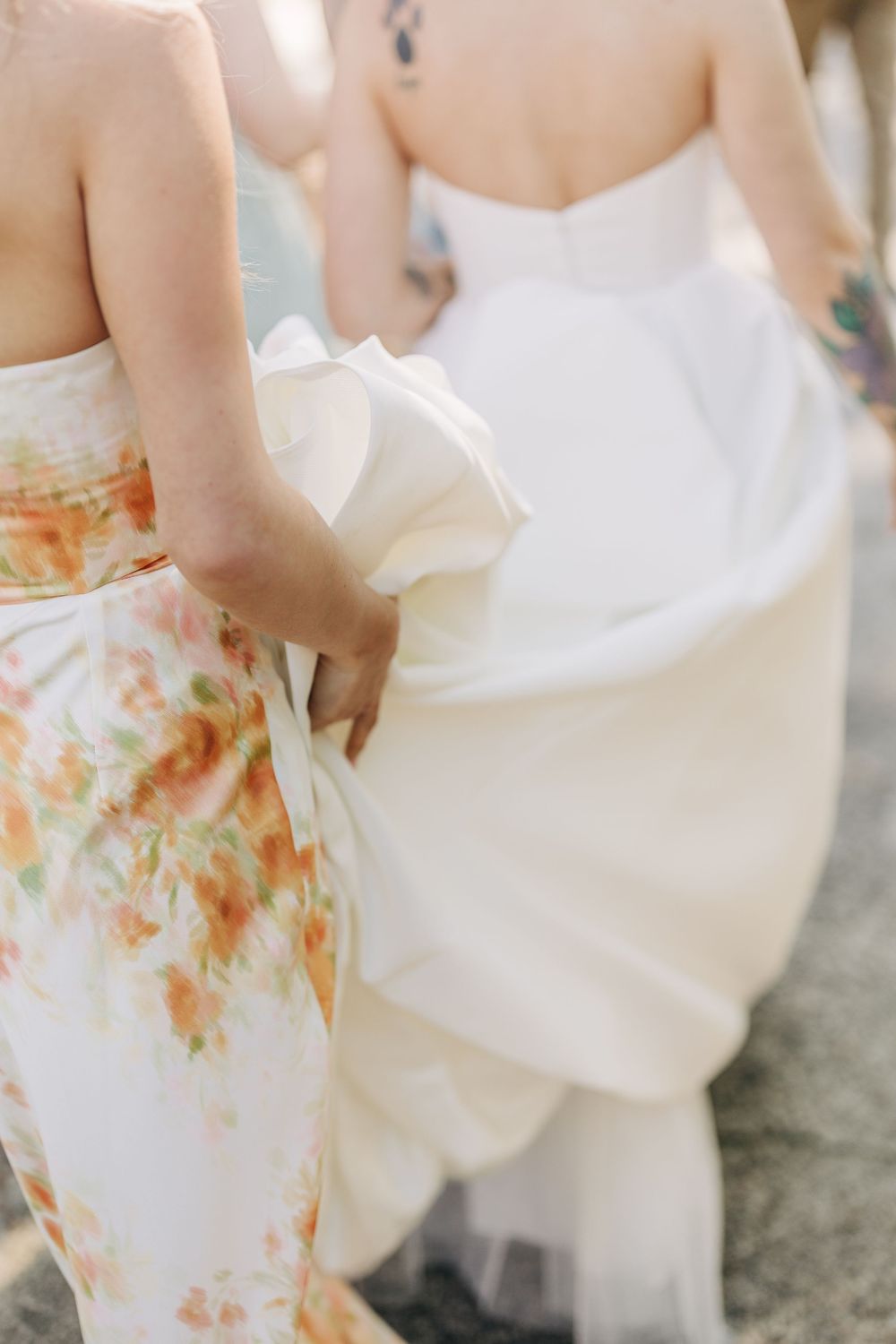 Bride in white gown held by bridesmaid in floral dress at outdoor wedding ceremony.