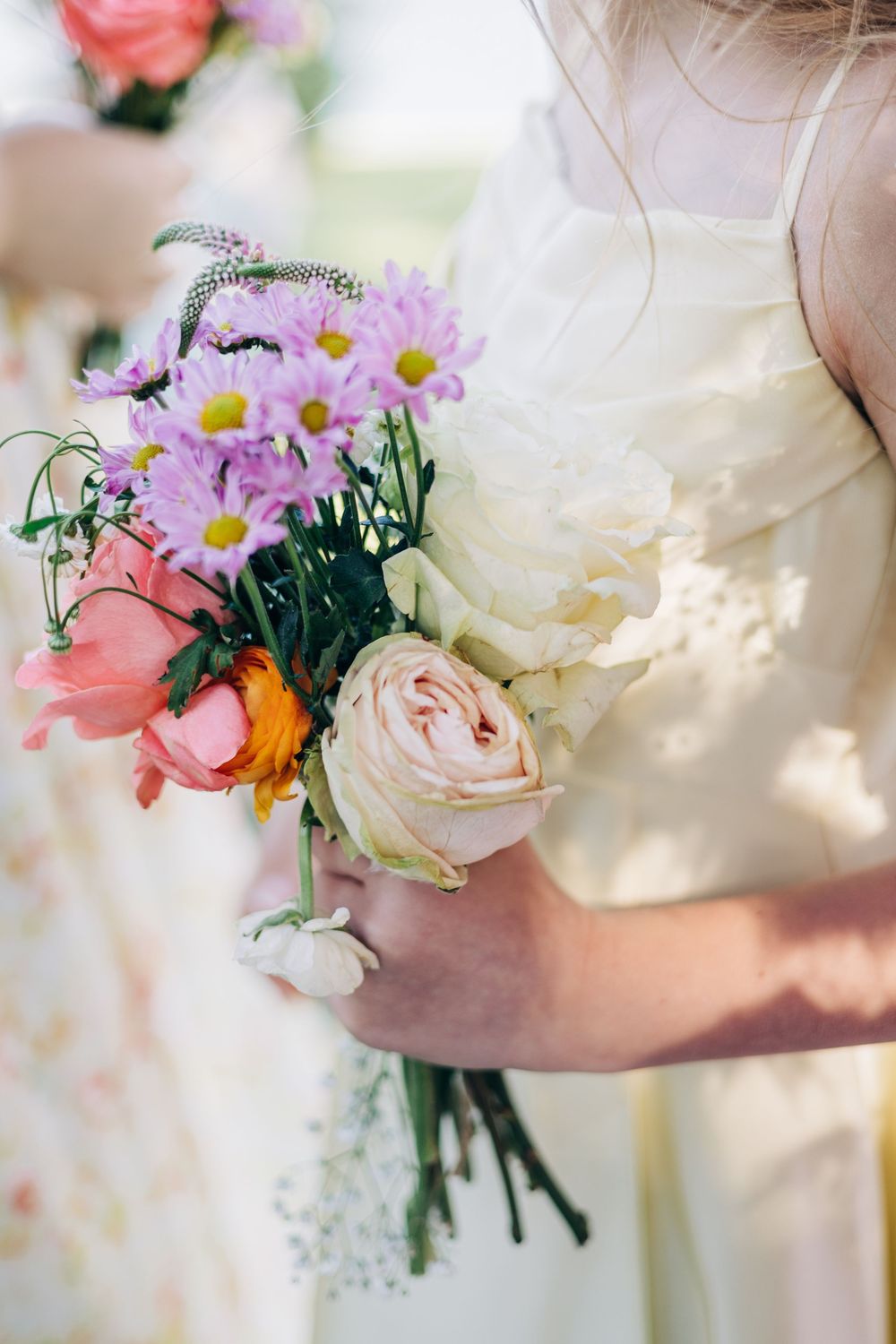 Bridesmaid in white dress holding a colorful wedding bouquet with pink roses, purple daisies, and orange flowers.