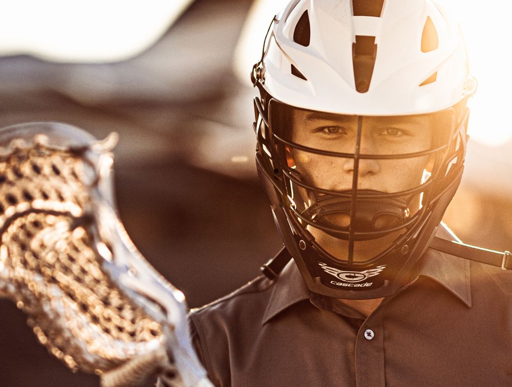 Close-up of athlete wearing white protective helmet with lacrosse stick at sunset.