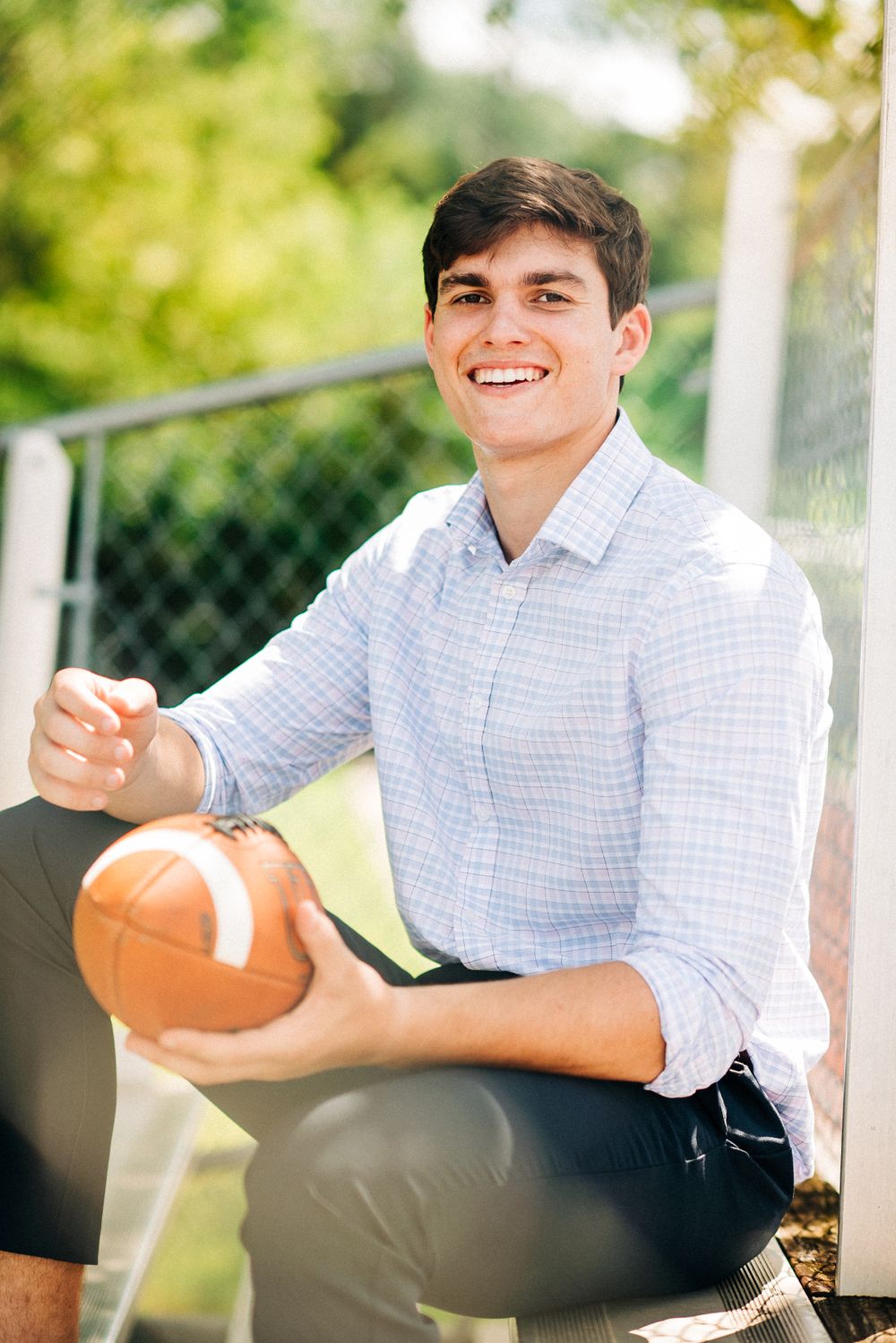 Athletic senior portrait outdoors holding football in button down shirt.