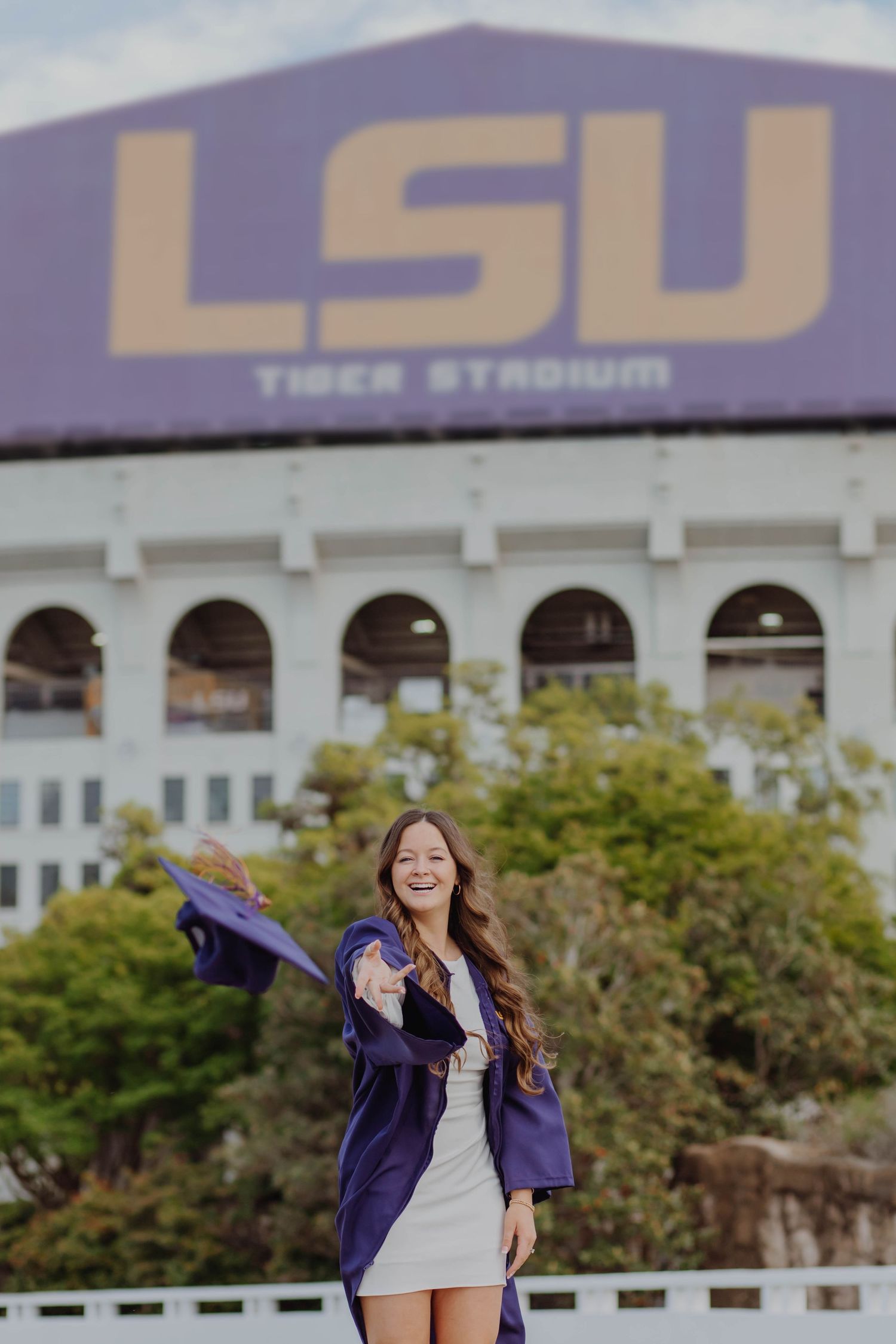 Graduate in purple gown celebrates in front of LSU Tiger Stadium.