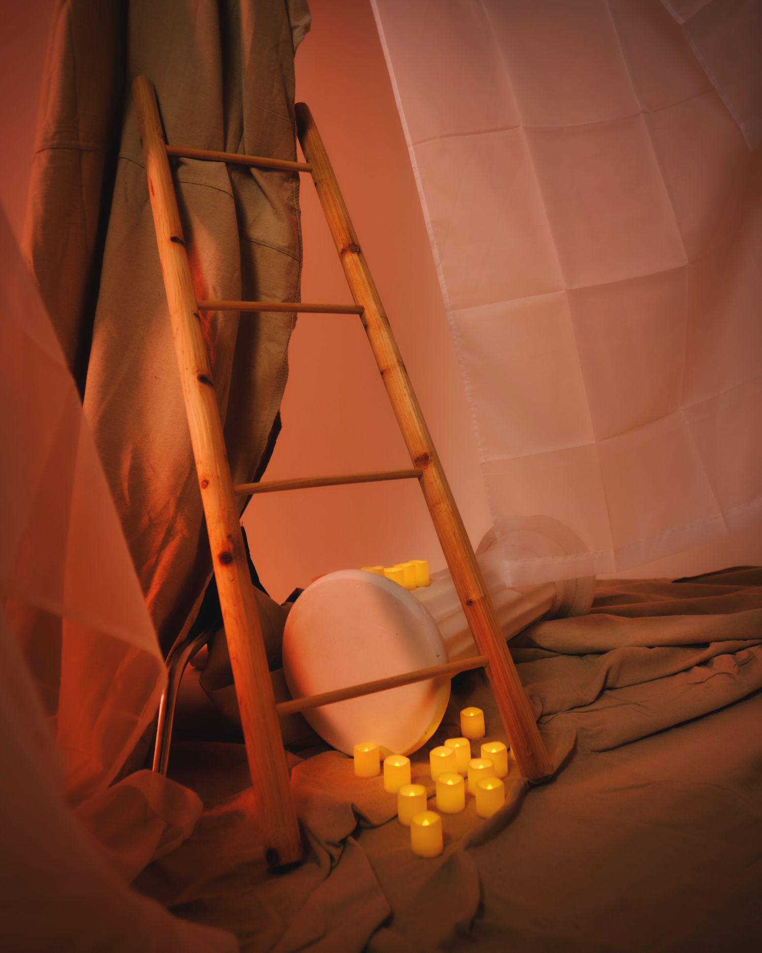 Artistic still life with ladder, construction helmet and glowing candles against orange wall.