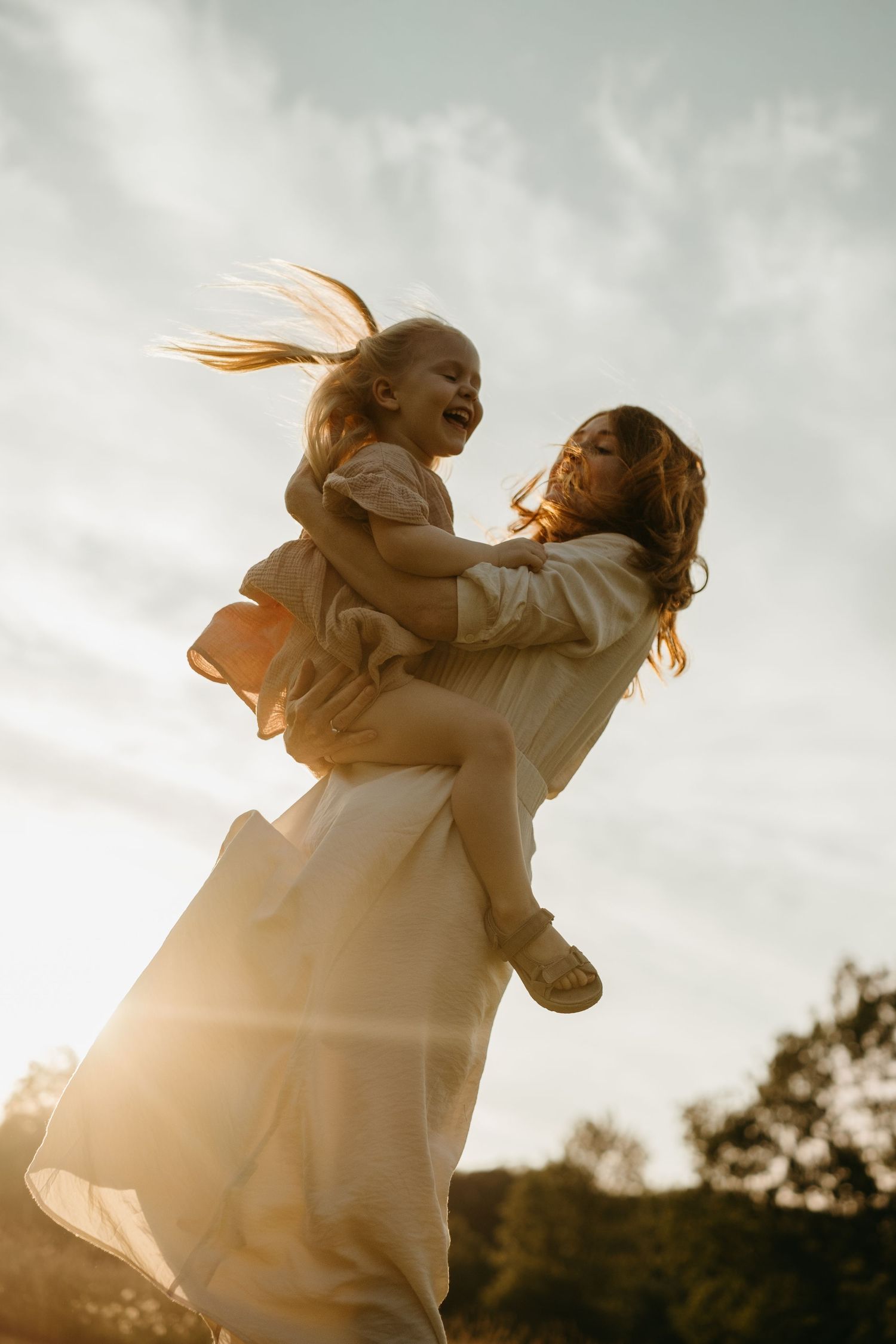 mother spinning her daughter in the air during sunset with their hair flying during unposed candid family photoshoot in Stockholm