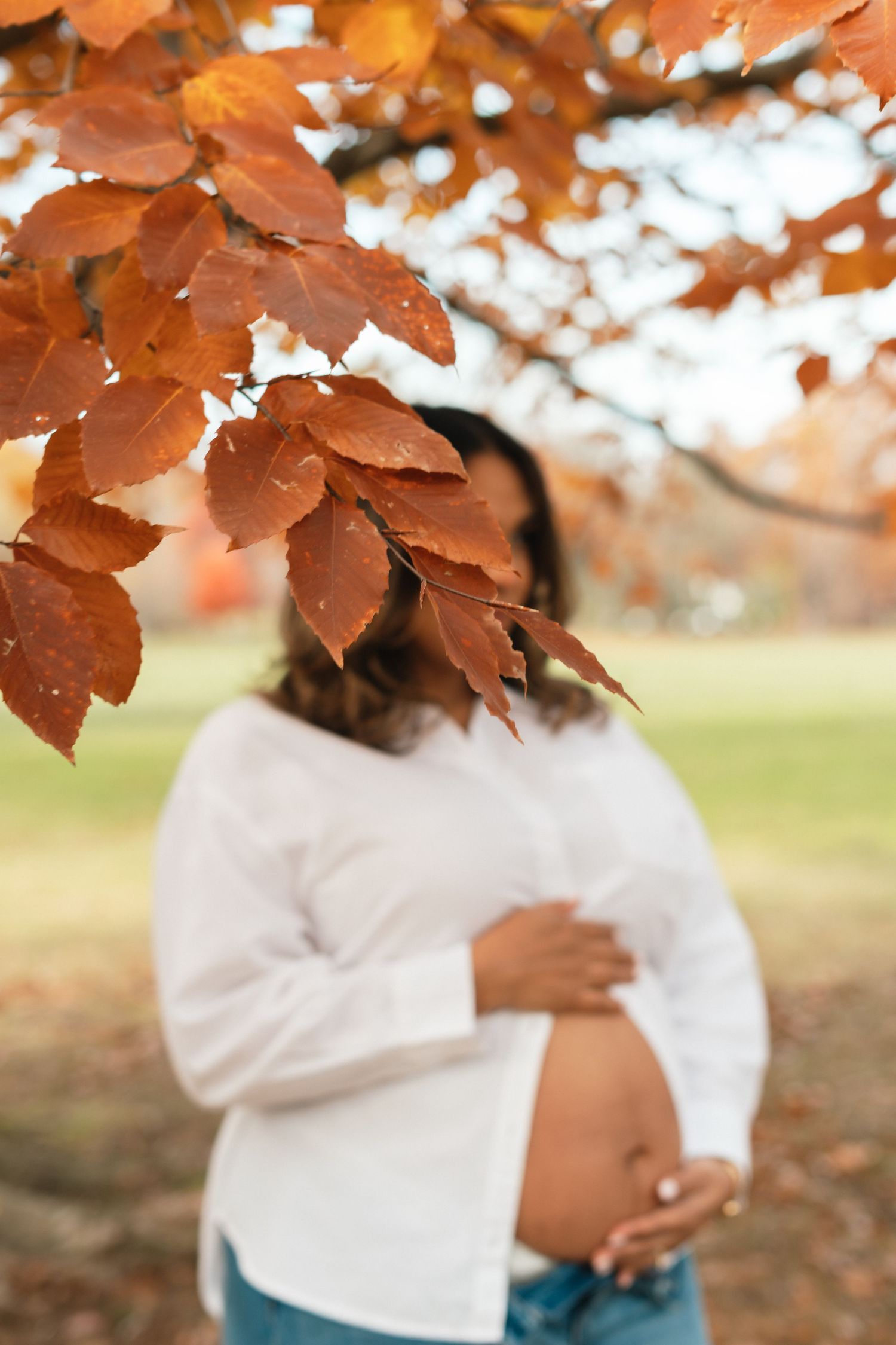 Autumn maternity photo under orange maple leaves in soft natural light.