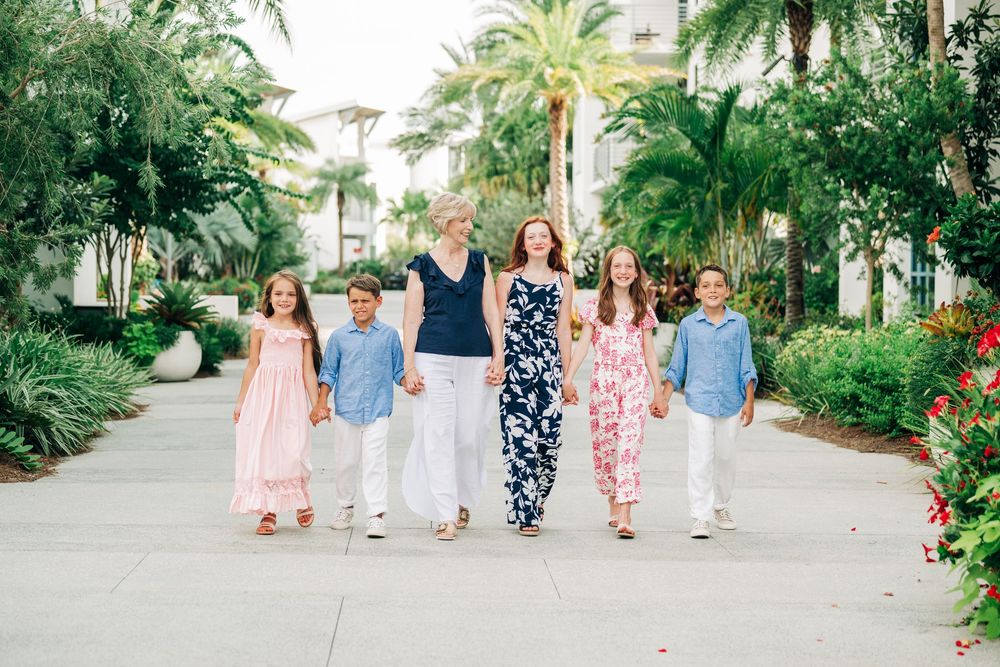 A group of people walking down a palm tree-lined path wearing coordinated pink, blue and floral summer outfits.