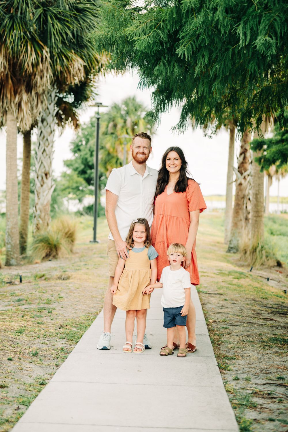 A family poses together on a palm-lined path in coordinated casual outfits.