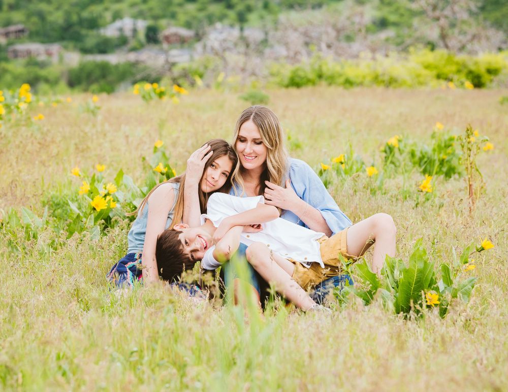 Family of three laughing and playing together in a sunny wildflower meadow with yellow blooms.