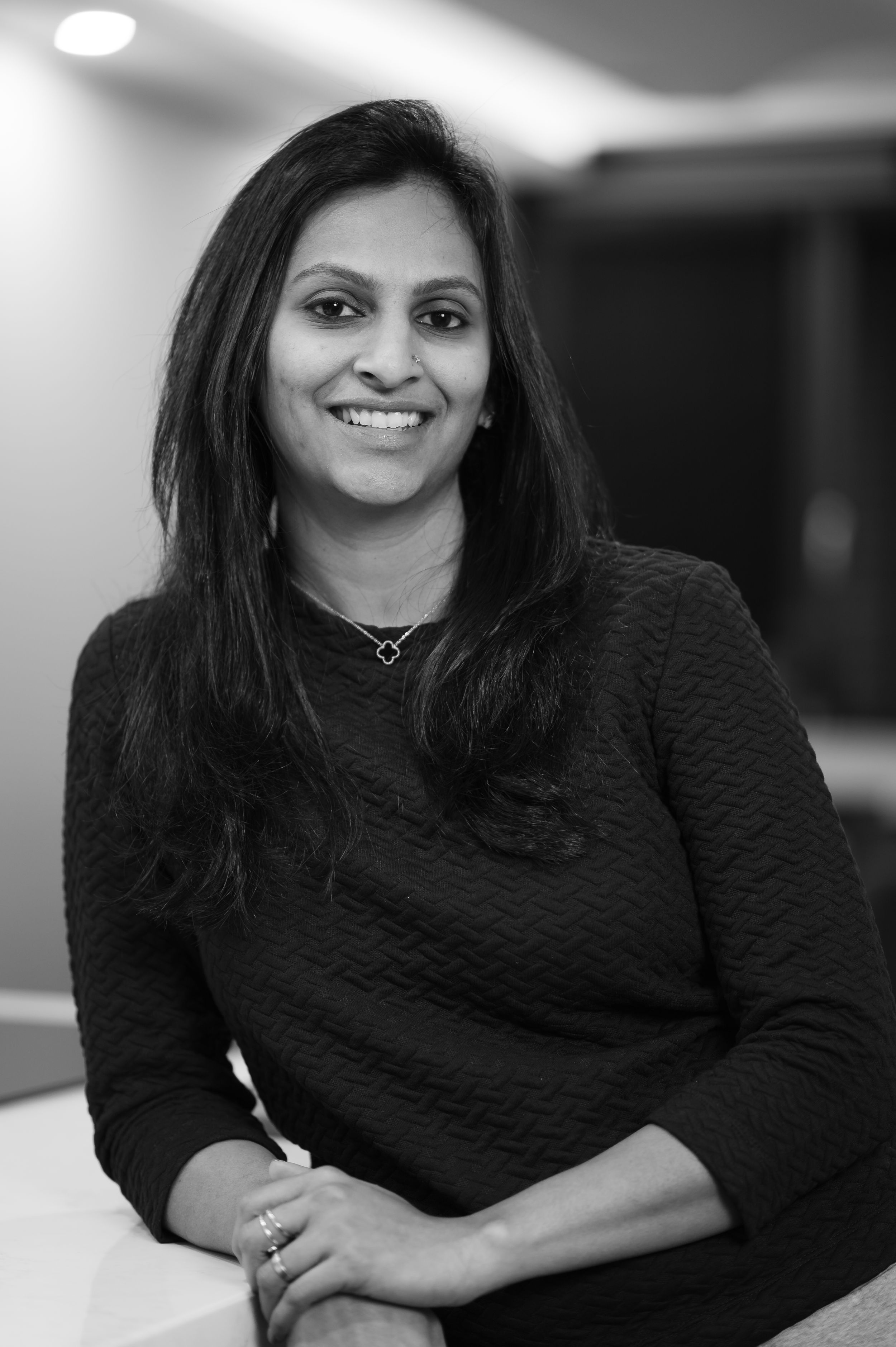 Black and white portrait of someone in a dark sweater smiling warmly at the camera.