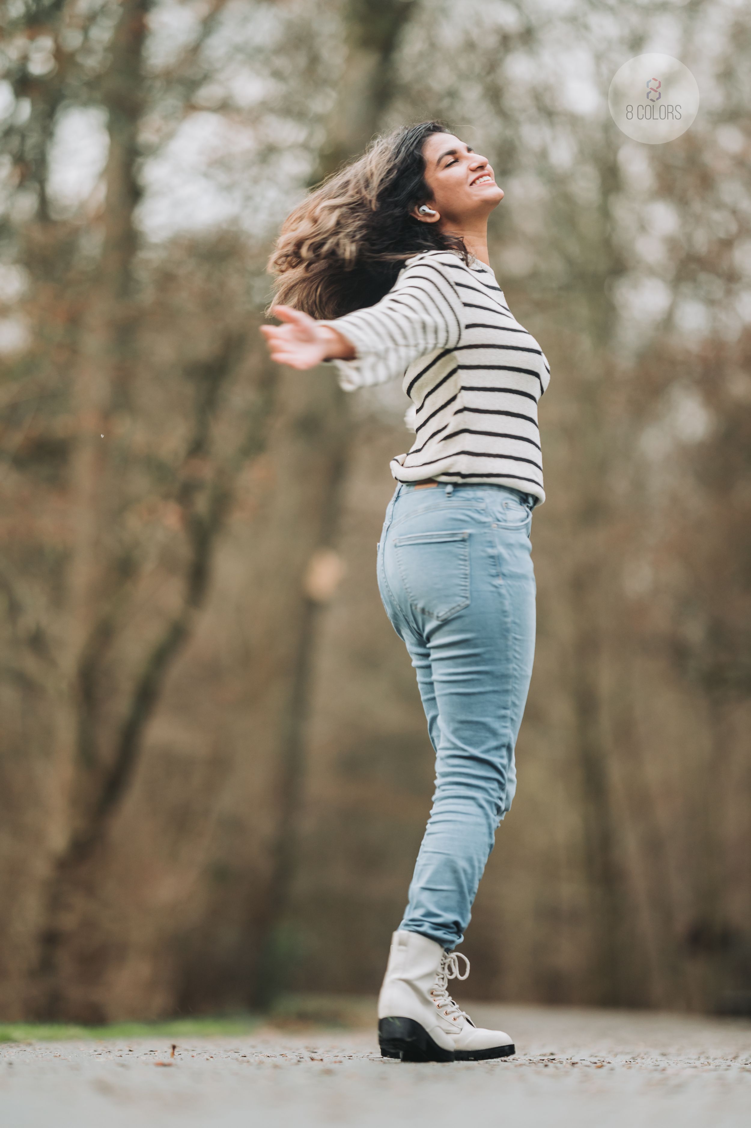 Dancing figure in a striped sweater and jeans strikes a joyful pose against a blurred forest backdrop.