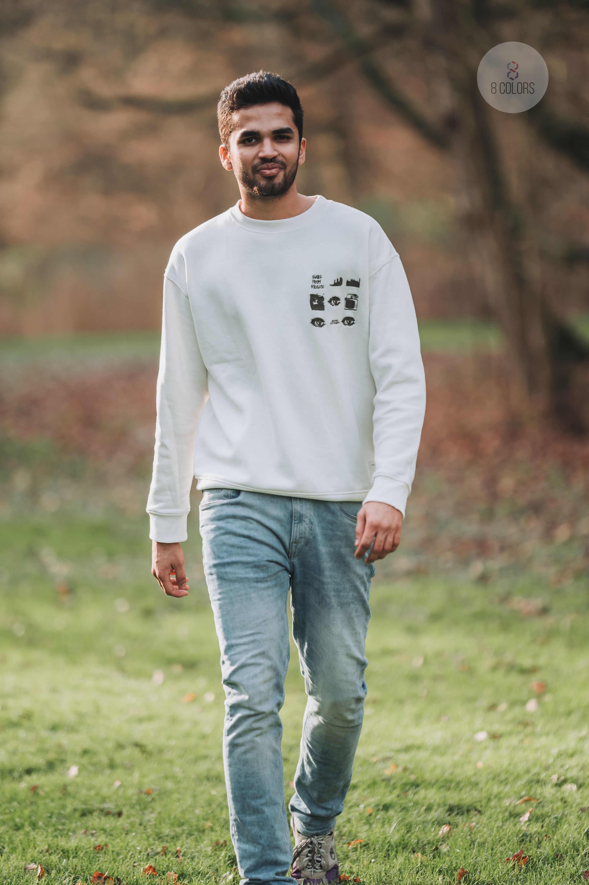 A casual outfit featuring a white crewneck sweatshirt with small graphic details paired with light wash denim jeans outdoors.