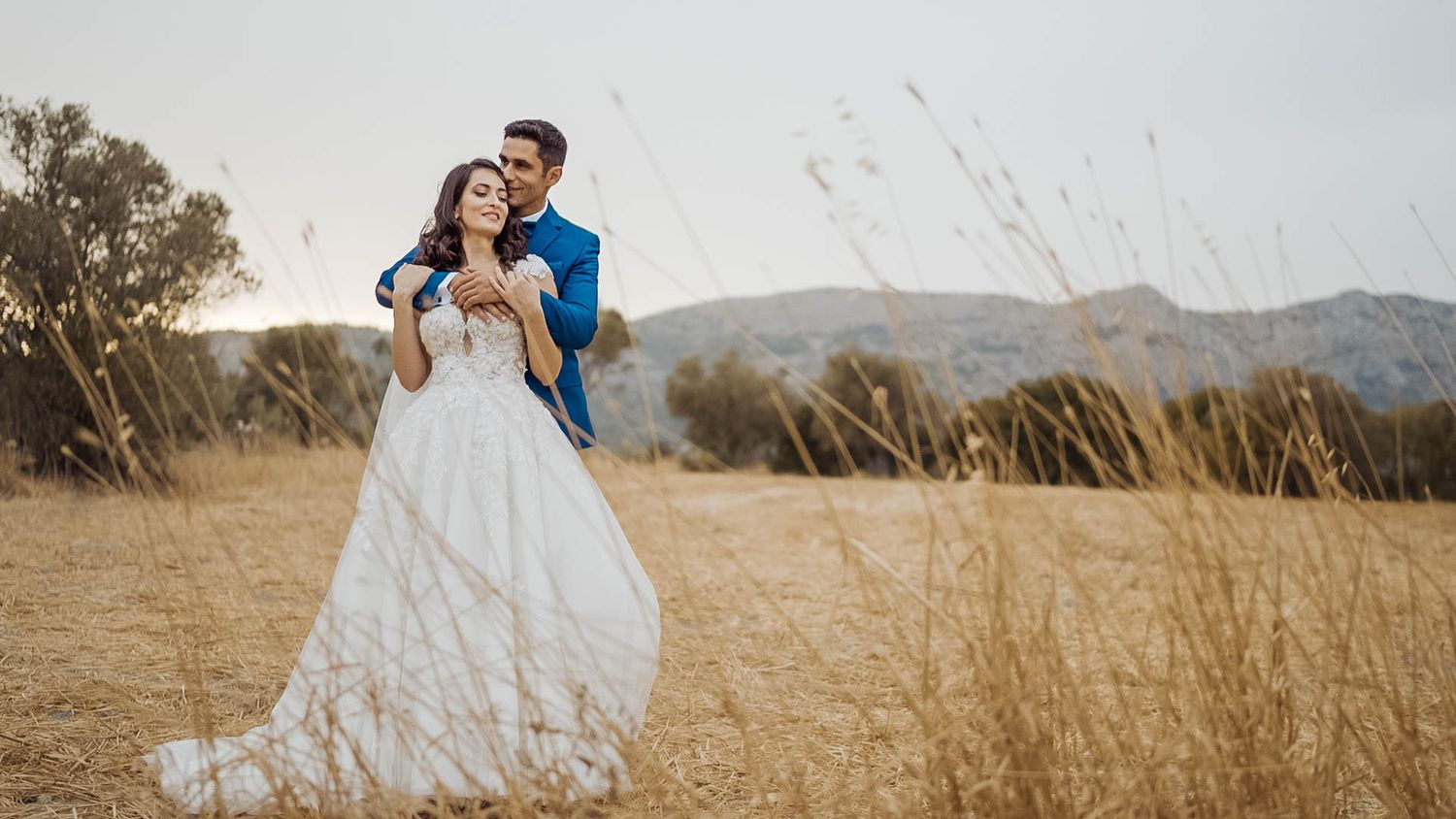 A romantic wedding portrait in a golden field with mountains in the background.