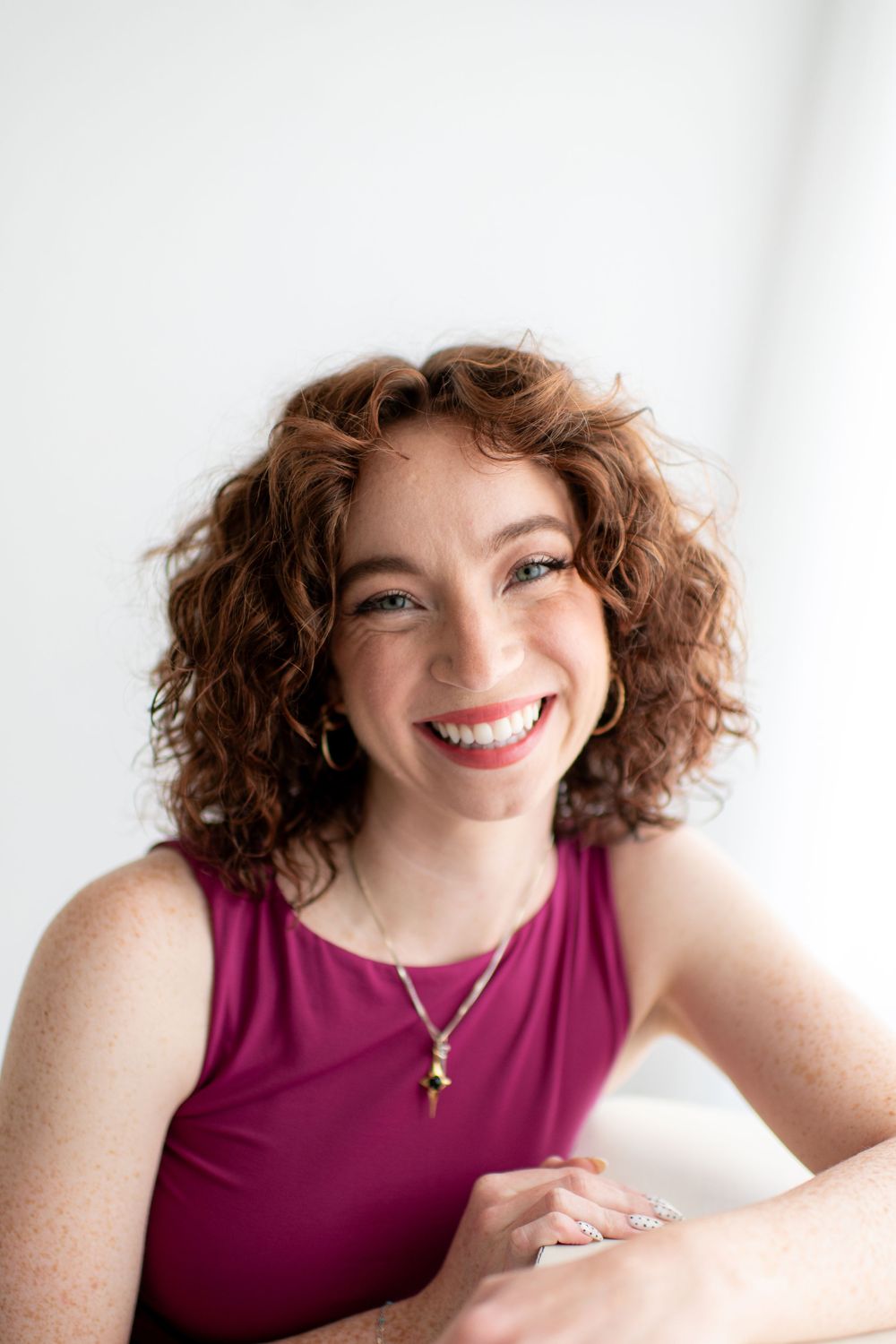 Professional headshots of a person in a burgundy sleeveless top with curly hair against a white background.