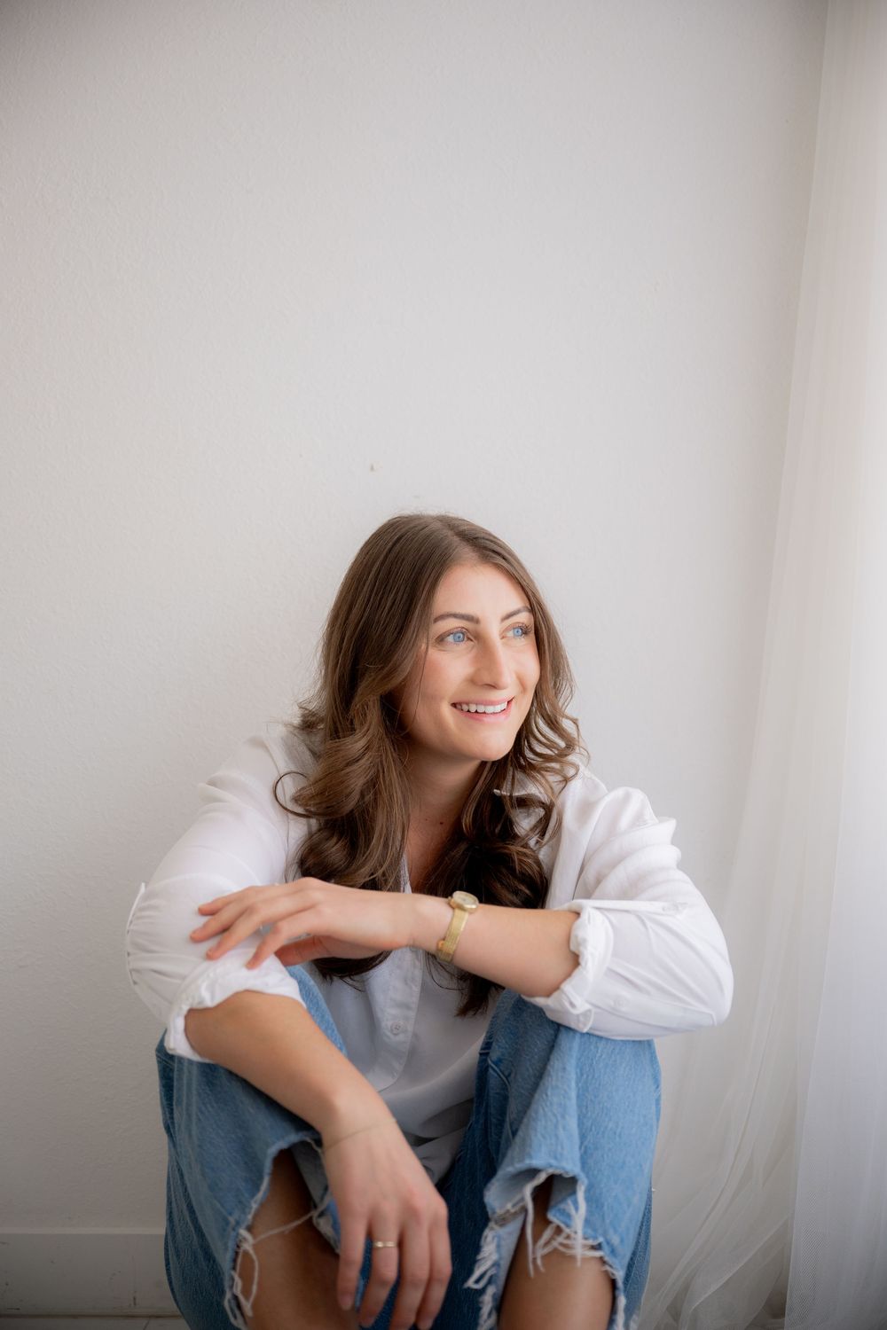 A sequence of casual lifestyle portraits showing a person in a white shirt and jeans sitting against a light wall.