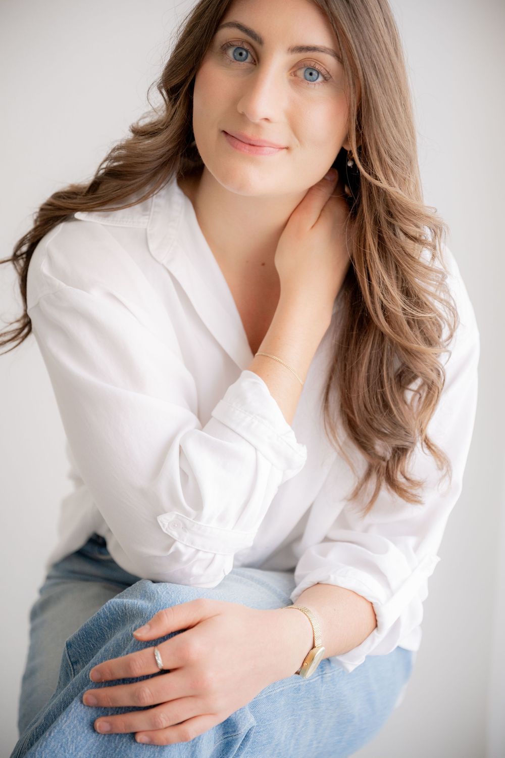 Portrait of someone in a casual white button-down shirt and blue jeans sitting against a light background.