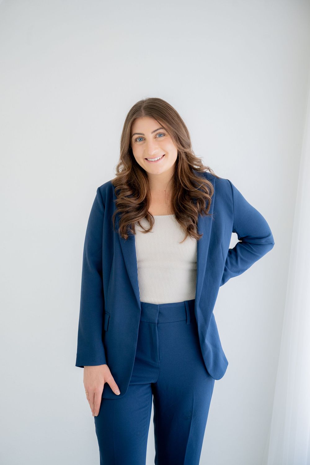 Professional woman in navy blue business suit and white top stands confidently against white background.
