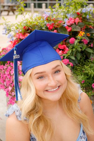 Graduation portraits with a blue cap against pink flowers and greenery.