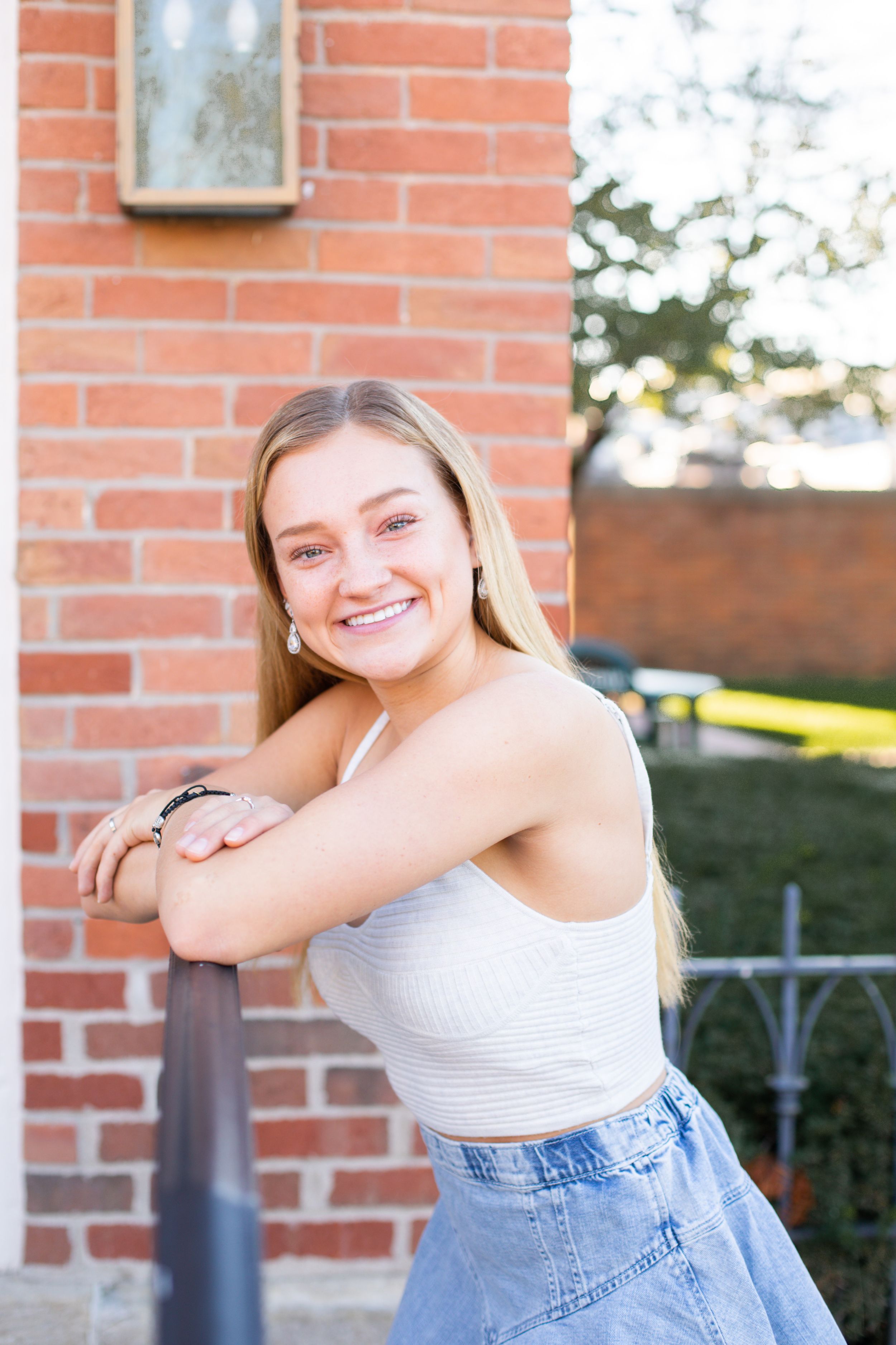 Casual portrait session against brick wall wearing white top and denim.
