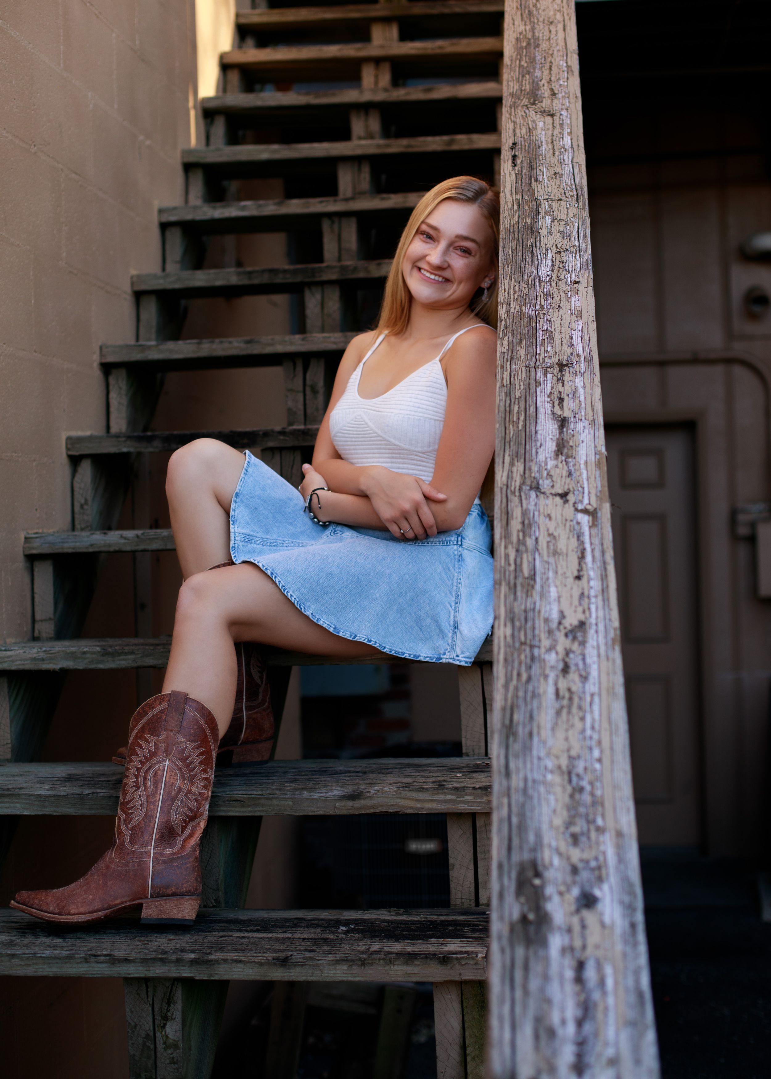 Portrait session on rustic wooden stairs wearing cowboy boots and denim skirt.