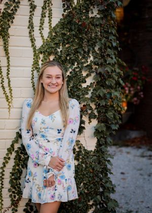 Fashion shoot with floral dress and climbing ivy wall background creating a garden aesthetic.