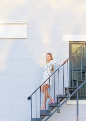 Person in white dress posing on outdoor metal staircase against white wall.