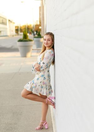 Playful fashion poses in a floral dress and pink heels against an urban backdrop.