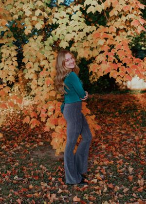 Portrait series against fall foliage wearing teal top and gray pants.