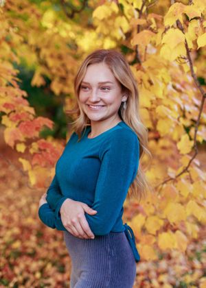 Autumn portrait session with golden leaves and a teal sweater.