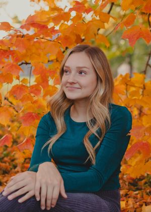 Casual autumn portrait featuring a teal sweater against bright orange maple leaves.