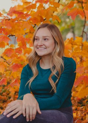 A teal sweater worn against vibrant orange autumn foliage in a seasonal portrait series.