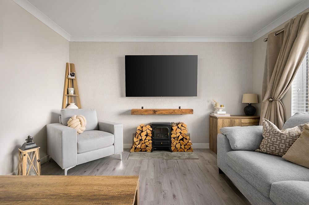 Modern living room with gray sofas, wall-mounted TV, stacked firewood, and light wood flooring.