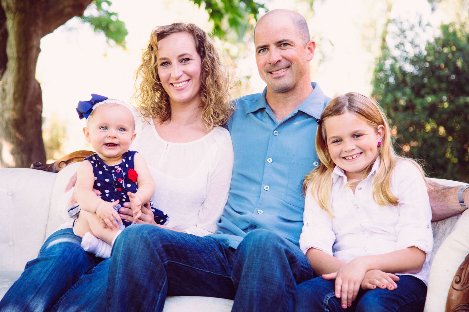 Family of four with infant girl and young girl wearing blue and white with infant wearing poke dot dress with red flower