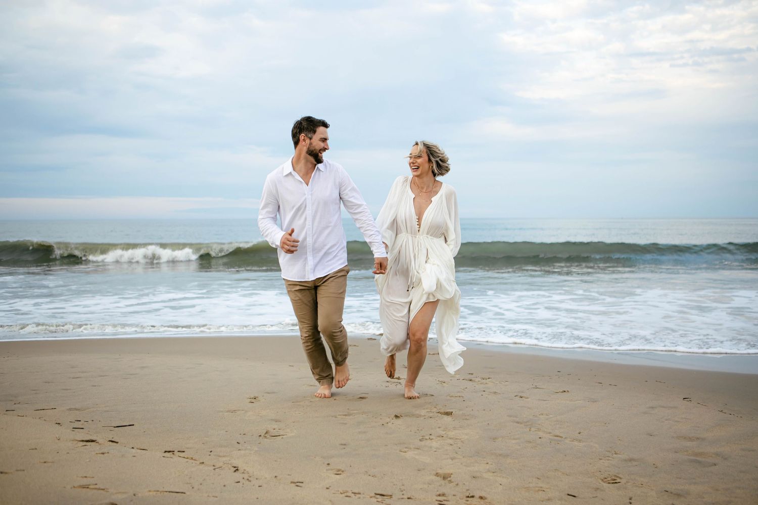 Romantic couple running and playing together along a sandy beach at sunset.