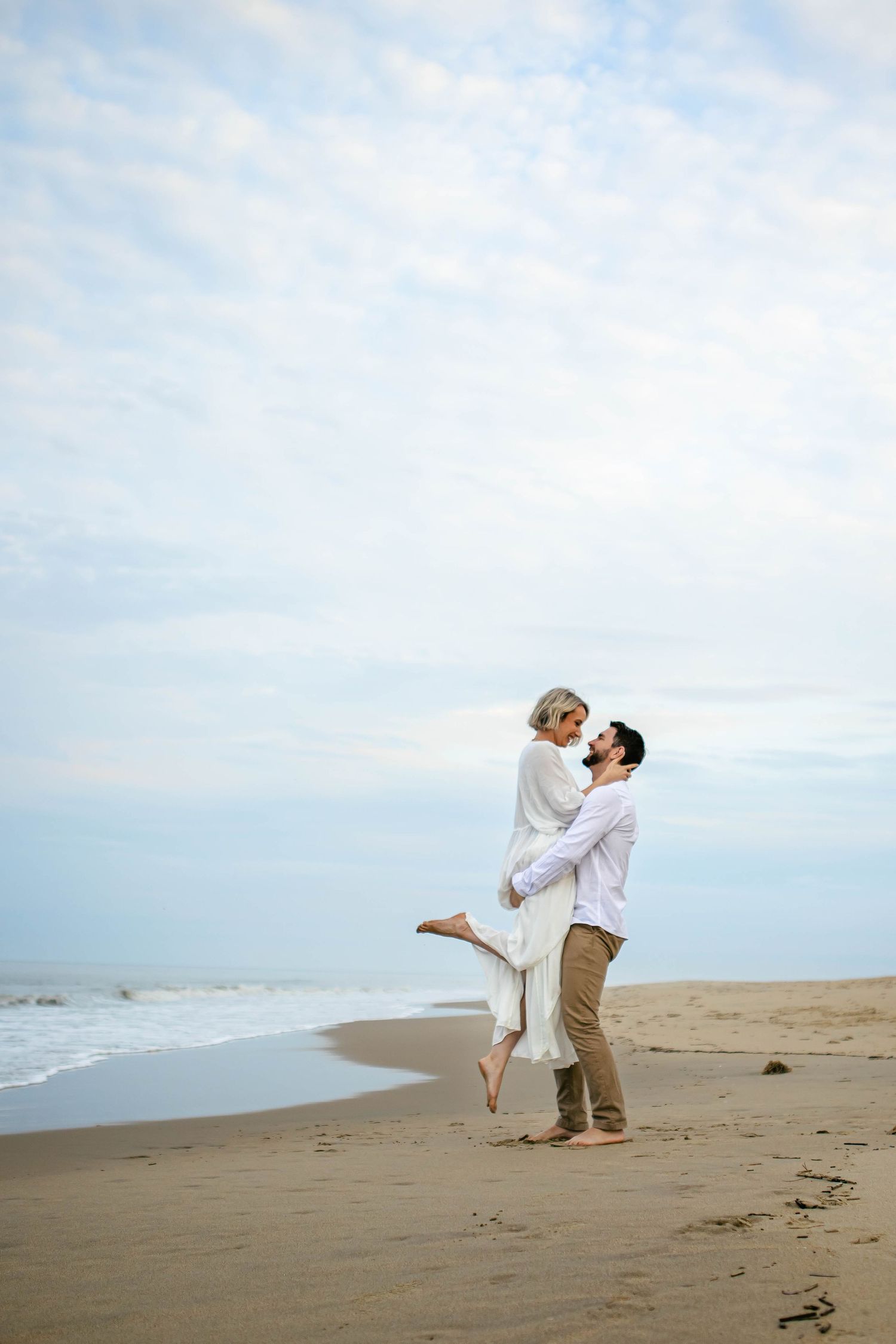 Couple dancing playfully on an empty beach with cloudy skies.