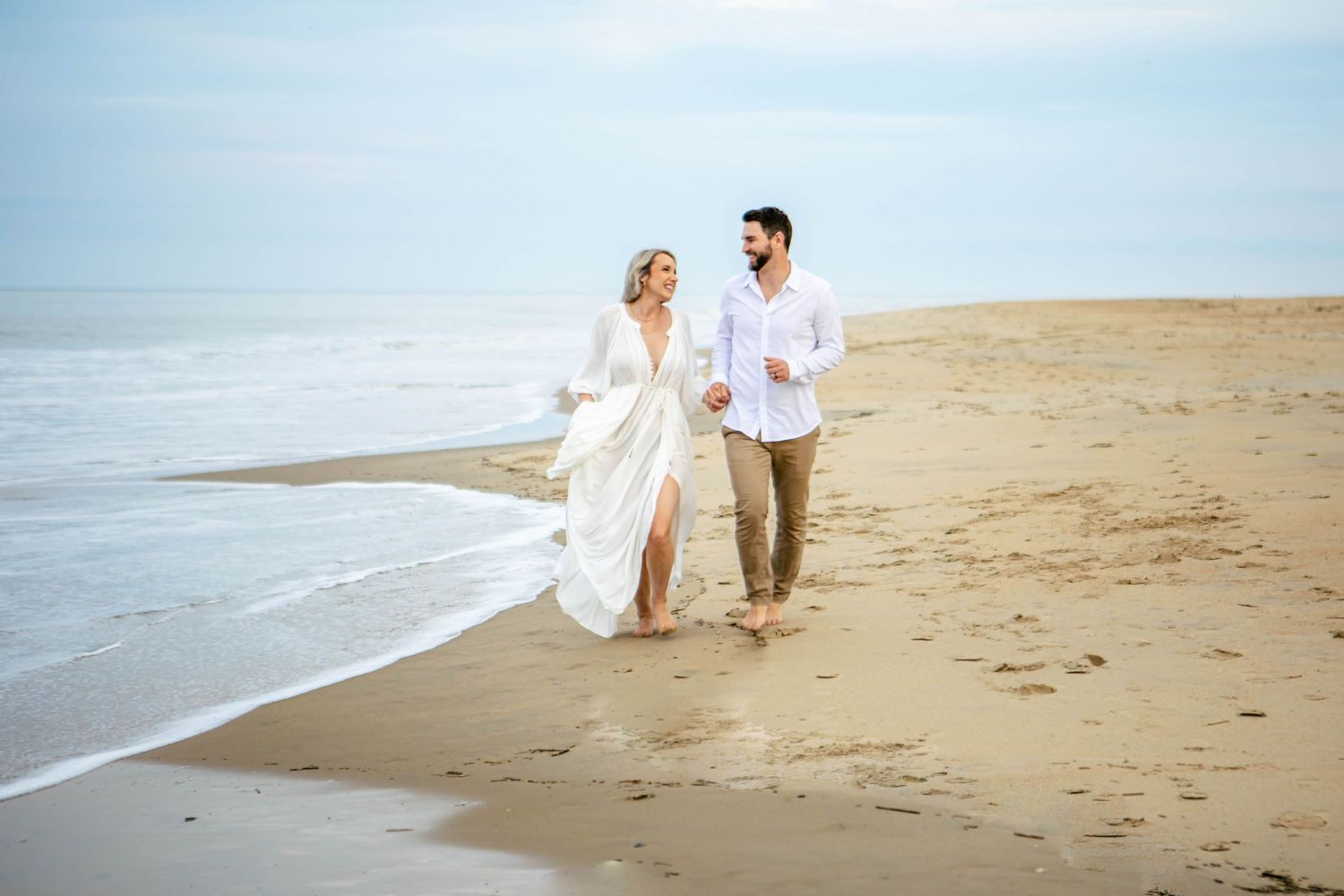 Couple walking and leaving footprints in the sand along a serene beach.