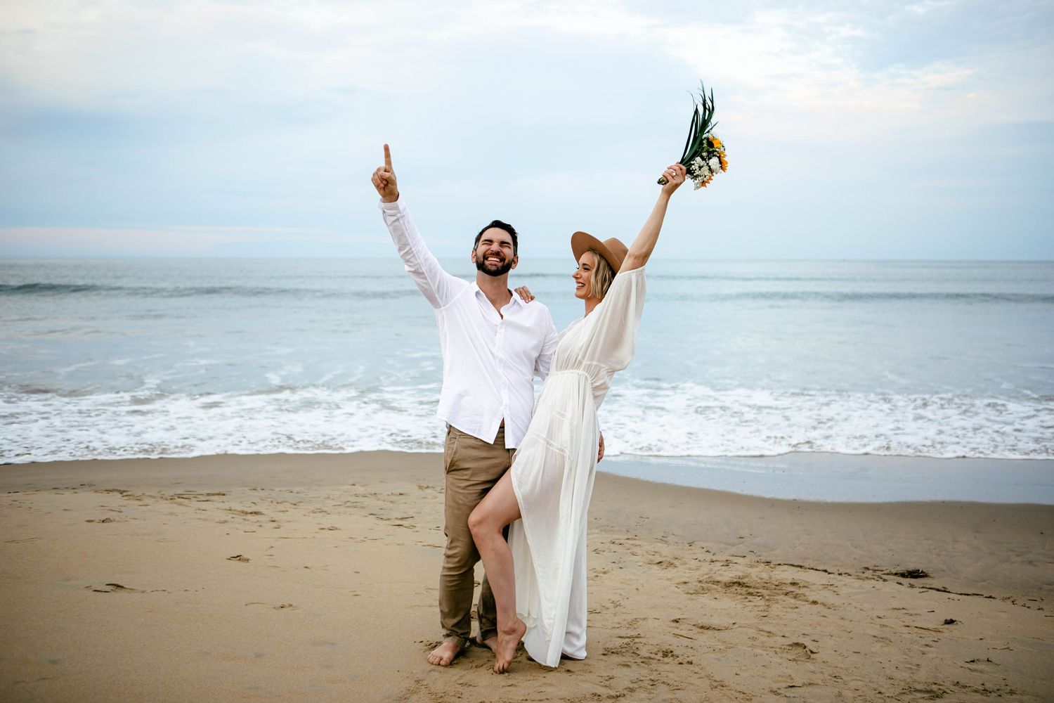 Joyful beach photoshoot with couple celebrating by the ocean waves.