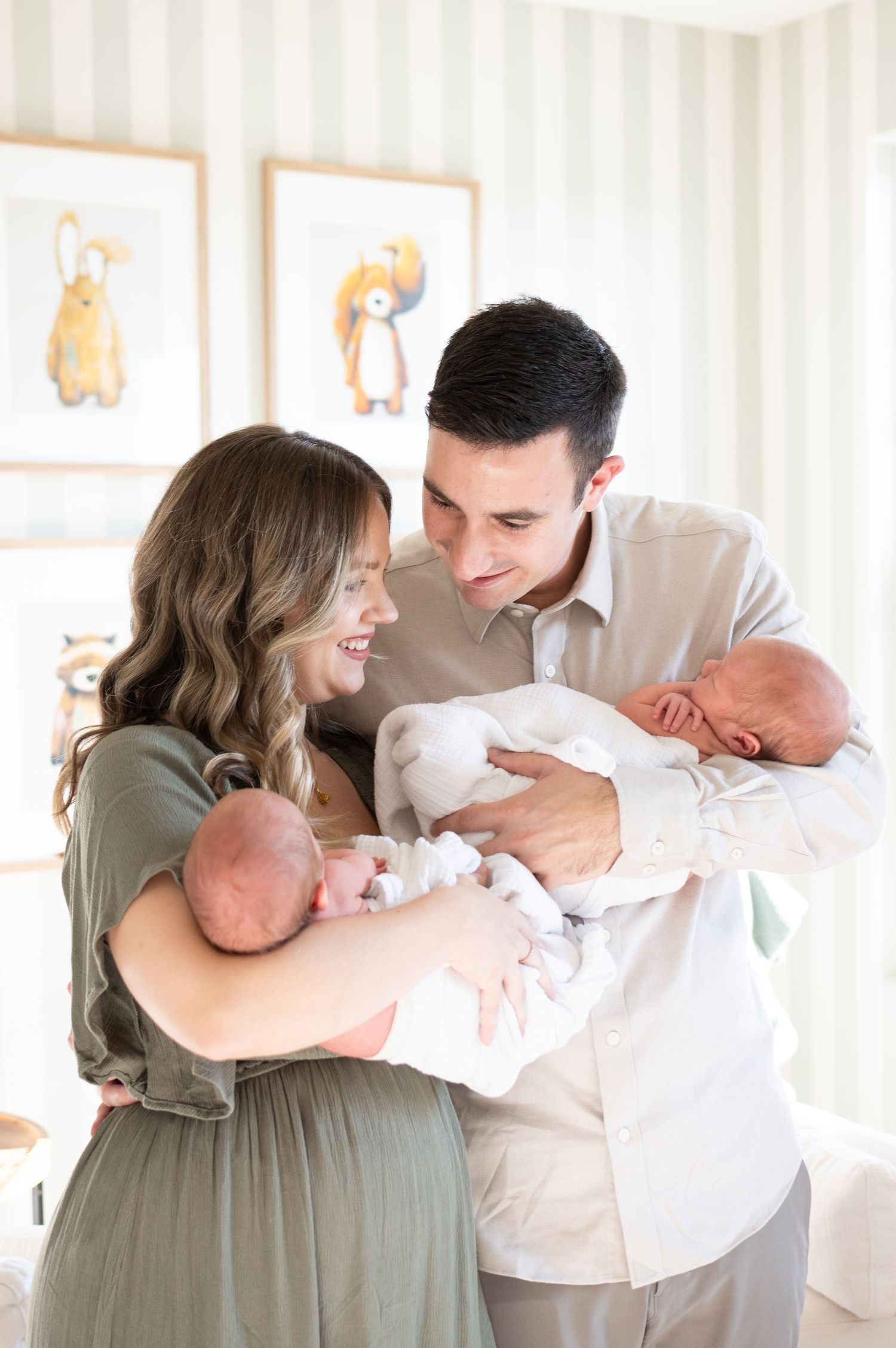 mom and dad in nursery, staring at their twin boys.  one baby in each parents arms while they look at opposite baby