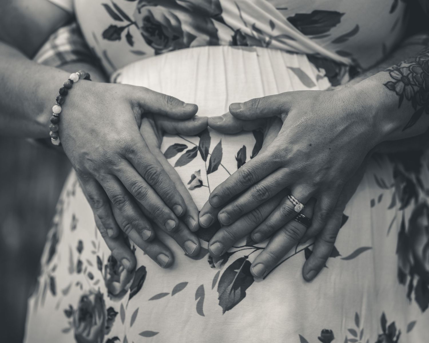 Black and white close-up of couple forming heart shape with hands on pregnant belly.
