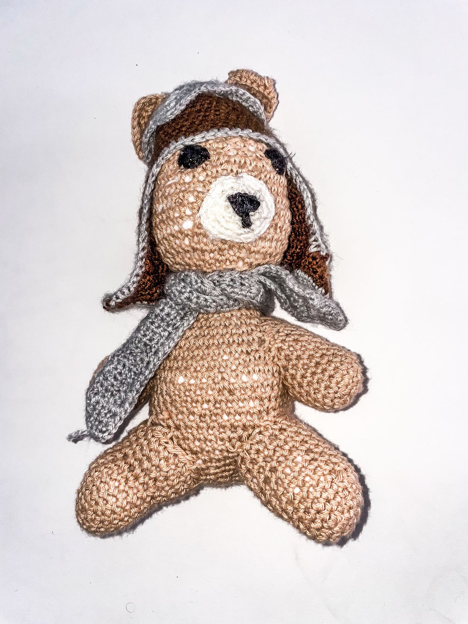 Handmade crochet teddy bear wearing a gray aviator hat with ear flaps.