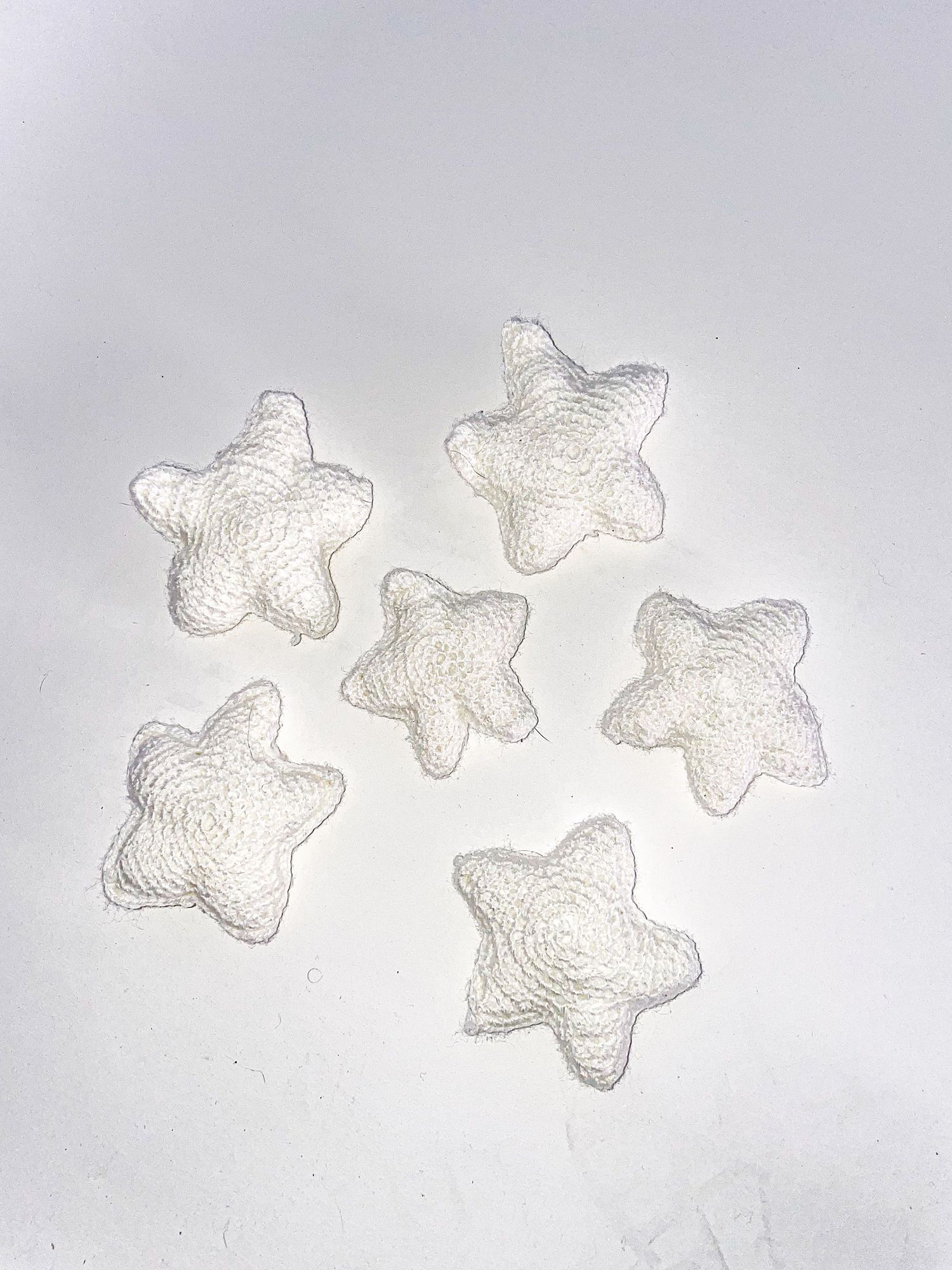 Set of six white crocheted star decorations arranged on light background.