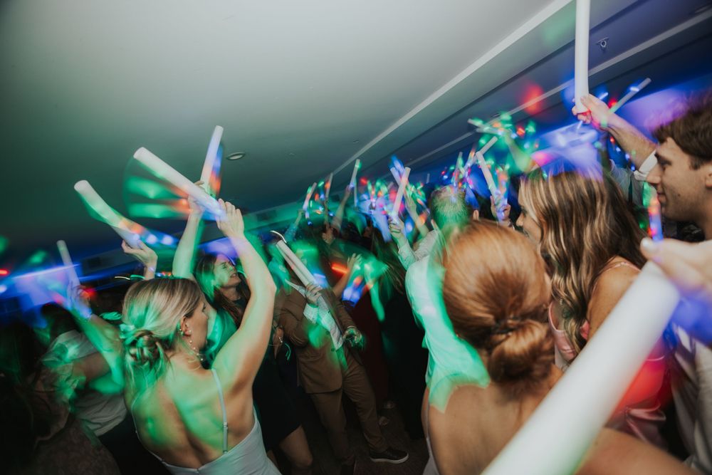 Crowd of party goers dancing at a wedding with green and blue lighting while holding glowsticks in the air in Maine.