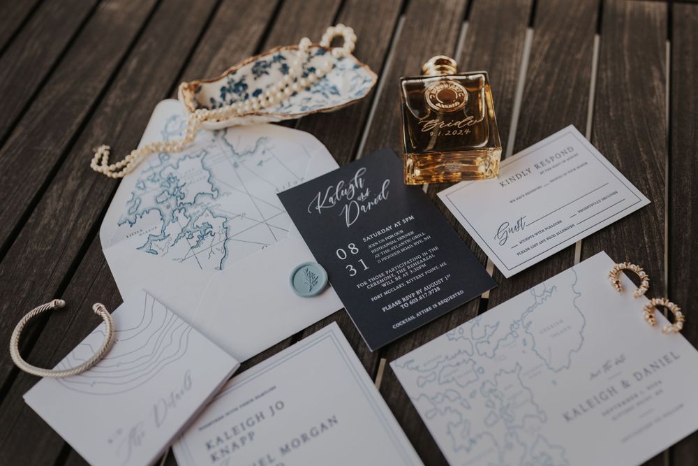 Wedding invitation suite with black and white stationery displayed on wooden deck with perfume bottle.