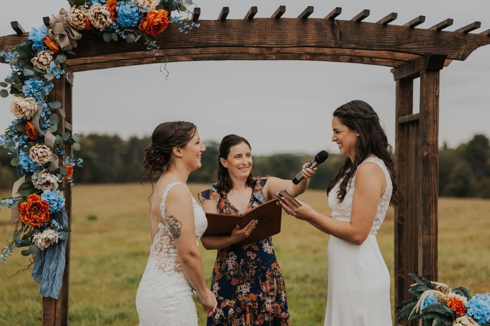 A wedding ceremony moment under a pergola adorned with vibrant blue and orange flowers.