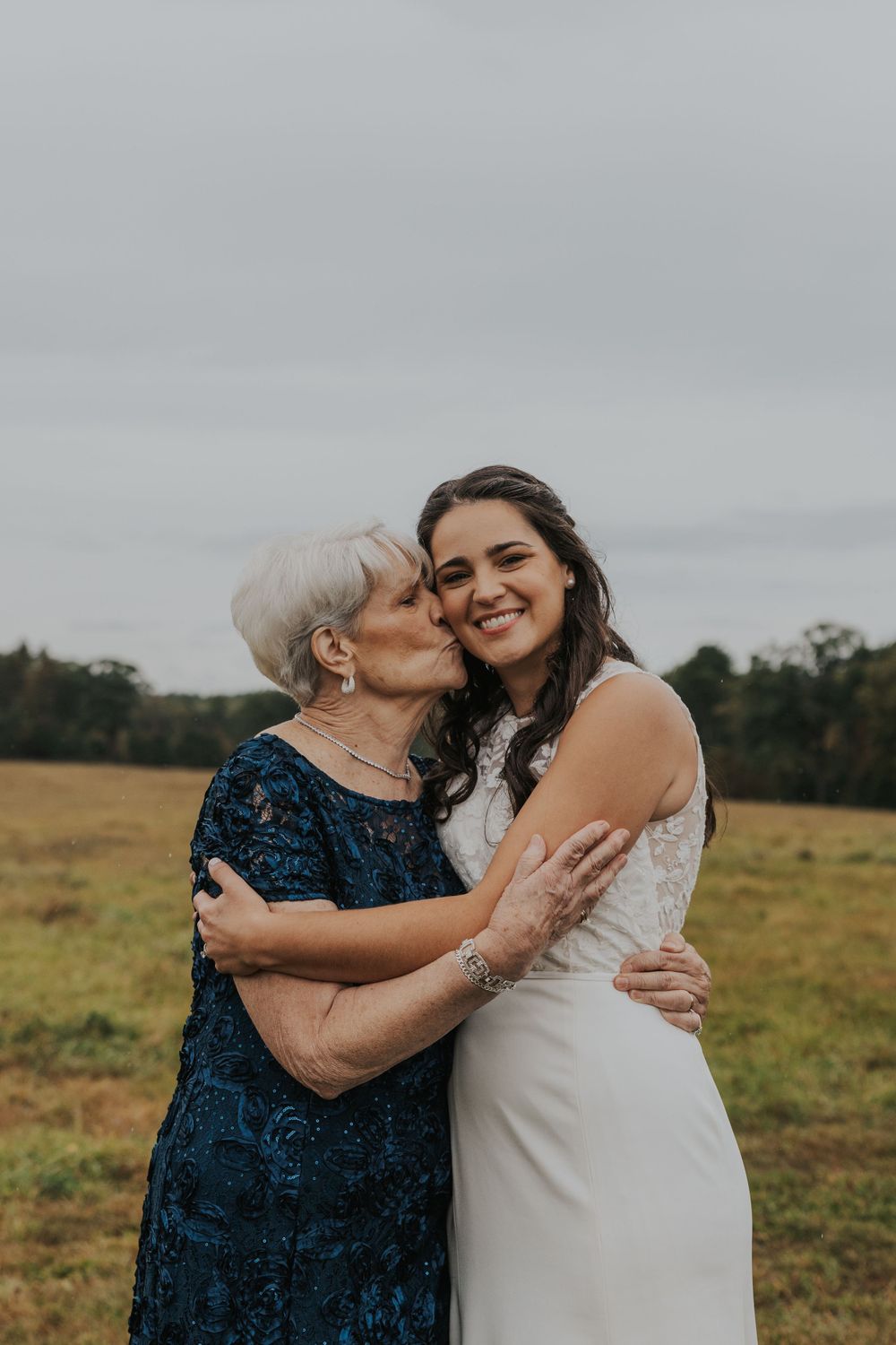 A tender embrace shared between two wedding guests against a rustic outdoor backdrop.