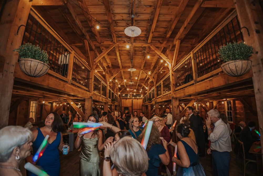 Wedding reception celebration in a rustic wooden barn with twinkling lights and dancing guests.