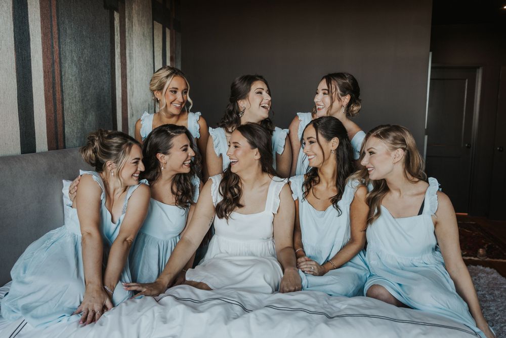 Bridal party wearing light blue dresses share joyful moment while sitting together during wedding festivities.